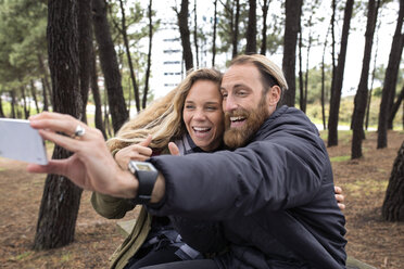 Cheerful couple taking selfie through smart phone in forest - CAVF40821