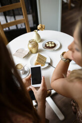 Overhead-Ansicht von Frauen, die ein Smartphone am Cafétisch benutzen - CAVF40826