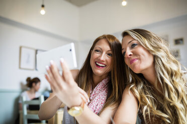 Cheerful female friends taking selfie through smart phone in cafe - CAVF40831