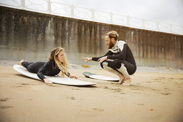 Man talking to woman lying on surfboard at beach - CAVF40837