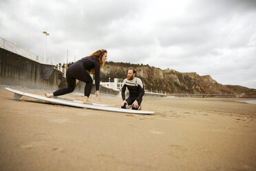 Man teaching surfing to woman at beach against cloudy sky - CAVF40838