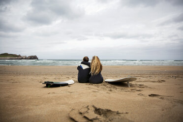 Rear view of couple sitting with surfboards at beach against sky - CAVF40839