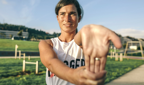 Woman stretching wrist while exercising at park stock photo