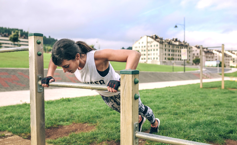 Woman doing push-ups on gymnastics bar at park stock photo