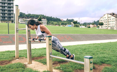 Side view of woman doing push-ups on gymnastics bar at park - CAVF40861