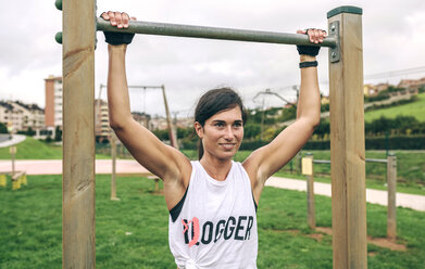 Confident woman holding gymnastics bar while exercising at park - CAVF40865