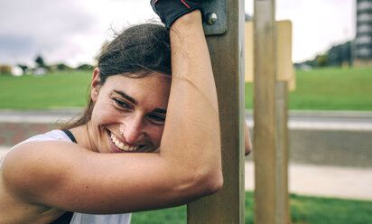 Glückliche Frau schaut weg, während sie sich im Park auf eine Gymnastikstange stützt - CAVF40875