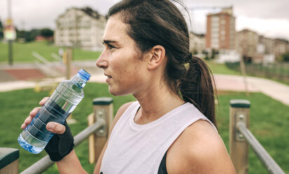 Woman looking away while holding water bottle at park - CAVF40876