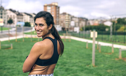 Porträt einer glücklichen Sportlerin, die im Park steht und über die Schulter schaut - CAVF40890