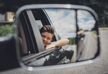 Reflection of cheerful boy seen in side-view mirror at car - CAVF40912