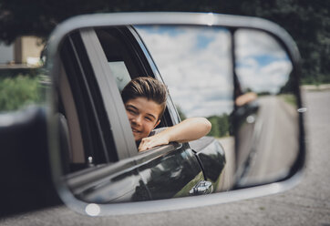 Spiegelung eines fröhlichen Jungen im Seitenspiegel eines Autos - CAVF40912