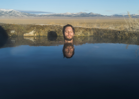 Mann mit geschlossenen Augen in ruhigem See gegen Himmel, lizenzfreies Stockfoto