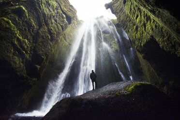 Niedriger Blickwinkel eines Mannes, der einen Wasserfall betrachtet, während er auf einer Felsformation steht - CAVF40949