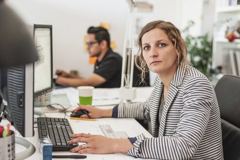 Porträt einer weiblichen Fachkraft mit einem Kollegen, der im Büro arbeitet - CAVF40983