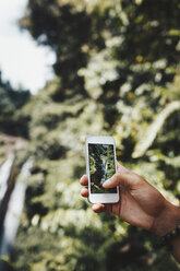 Cropped image of man photographing waterfall in forest - CAVF41245