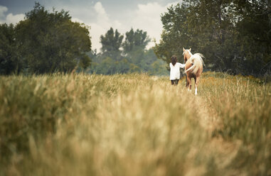 Rear view woman and horse walking on grassy field at countryside - CAVF41257