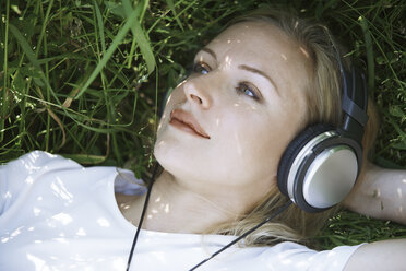 Thoughtful woman listening music while lying on grassy field - CAVF41273