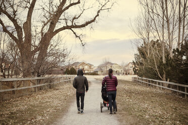 Rear view of man and woman walking with baby stroller on road during winter - CAVF41330