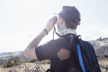 Wanderer, der durch ein Fernglas schaut, während er auf einem Berg gegen den Himmel an einem sonnigen Tag steht - CAVF41335