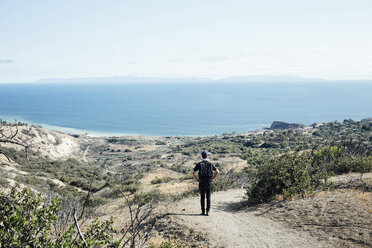 Rückansicht eines Wanderers, der die Aussicht betrachtet, während er auf einem Hügel gegen den Himmel an einem sonnigen Tag steht - CAVF41336