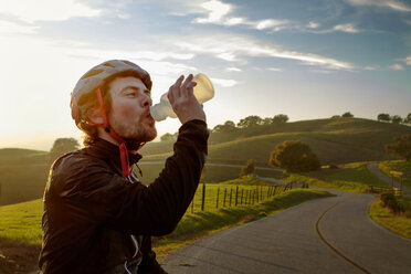 Mann trägt Helm und trinkt Wasser gegen den Himmel - CAVF41341