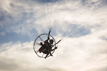 Low angle view of man paragliding against cloudy sky - CAVF41381