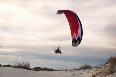 Mann Gleitschirmfliegen über Strand gegen bewölkten Himmel - CAVF41382