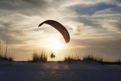 Mann Gleitschirmfliegen über Sand gegen bewölkten Himmel bei Sonnenuntergang - CAVF41386