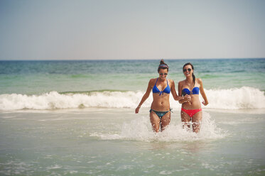 Cheerful sisters walking in sea against clear sky - CAVF41395