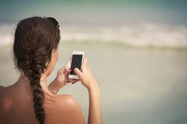 Rückansicht einer Frau mit geflochtenen Haaren beim Telefonieren am Strand - CAVF41399