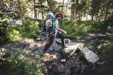 Female hiker crossing stream in forest - CAVF41404