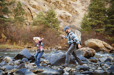 Vater und Sohn wandern auf Felsen inmitten eines Flusses am Berg - CAVF41415