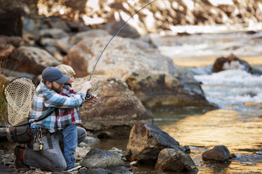 Father and son fishing by river in forest - CAVF41418