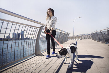 Lächelnde Frau, die mit ihrem Hund am Geländer einer Brücke spazieren geht, bei klarem Himmel - CAVF41499