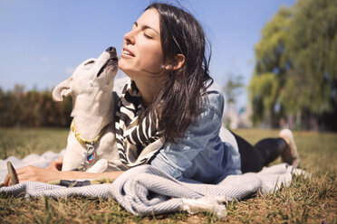 Loving woman and dog lying on blanket at park - CAVF41509