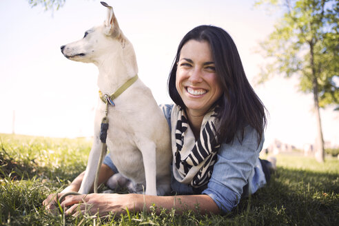 Porträt einer lächelnden Frau, die mit ihrem Hund auf einer Wiese im Park liegt - CAVF41512