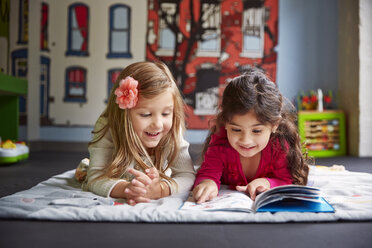 Glückliche Freunde lesen ein Buch und liegen auf einer Decke in der Kinderbetreuung - CAVF41523