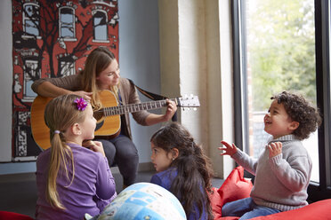 Lehrerin spielt Gitarre, während die Kinder in der Vorschule Spaß haben - CAVF41549