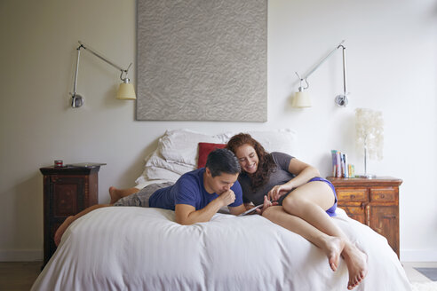 Paar schaut auf Tablet-Computer, während sie auf dem Bett im Schlafzimmer liegen - CAVF41552