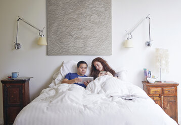 Paar schaut auf Tablet-Computer, während es auf dem Bett im Haus liegt - CAVF41553