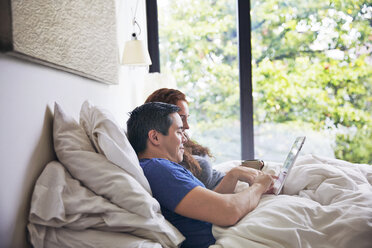 Seitenansicht eines Paares, das einen Tablet-Computer benutzt, während es zu Hause auf dem Bett liegt - CAVF41556