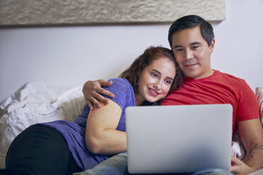 Loving couple looking at laptop computer while lying on bed at home - CAVF41579