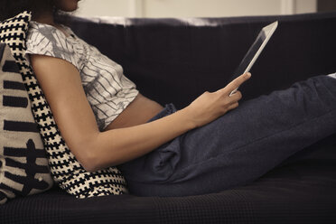 Midsection of woman using tablet computer while reclining on sofa at home - CAVF41592