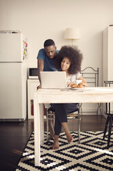 Couple using laptop computer at table with croissants in kitchen - CAVF41598