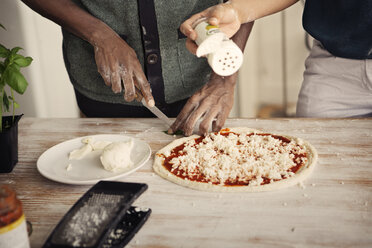 Midsection of couple preparing pizza while standing at kitchen table - CAVF41617