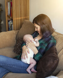 Woman breastfeeding daughter while sitting on sofa at home - CAVF41647