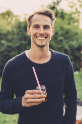 Portrait of happy man holding elderflower drink on roof garden - MASF04696