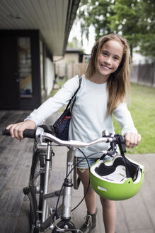 Porträt eines glücklichen Mädchens, das mit dem Fahrrad vor dem Haus spazieren geht - MASF04699
