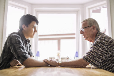 Side view of grandfather consoling grandson at table - MASF04755