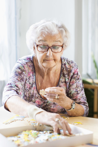 Ältere Frau beim Zusammensetzen von Puzzleteilen am Tisch im Pflegeheim, lizenzfreies Stockfoto